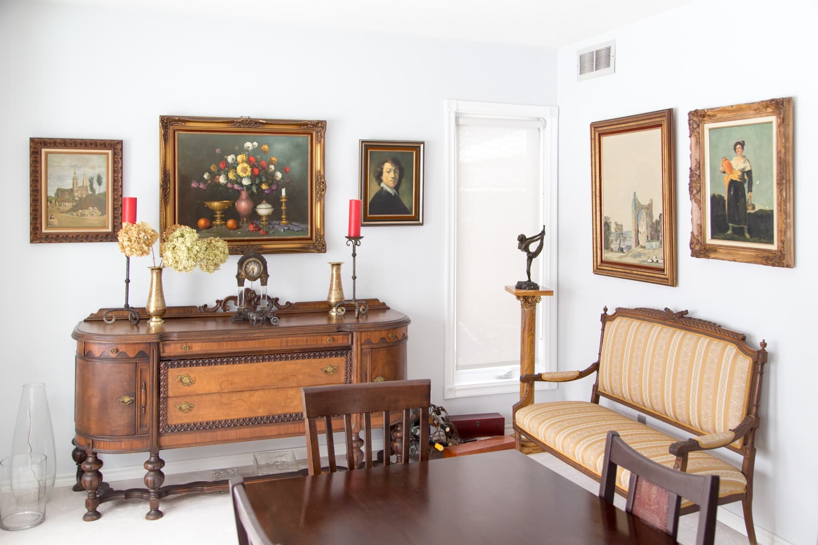 The dining room, with an antique walnut sideboard beneath a wall of framed oil paintings