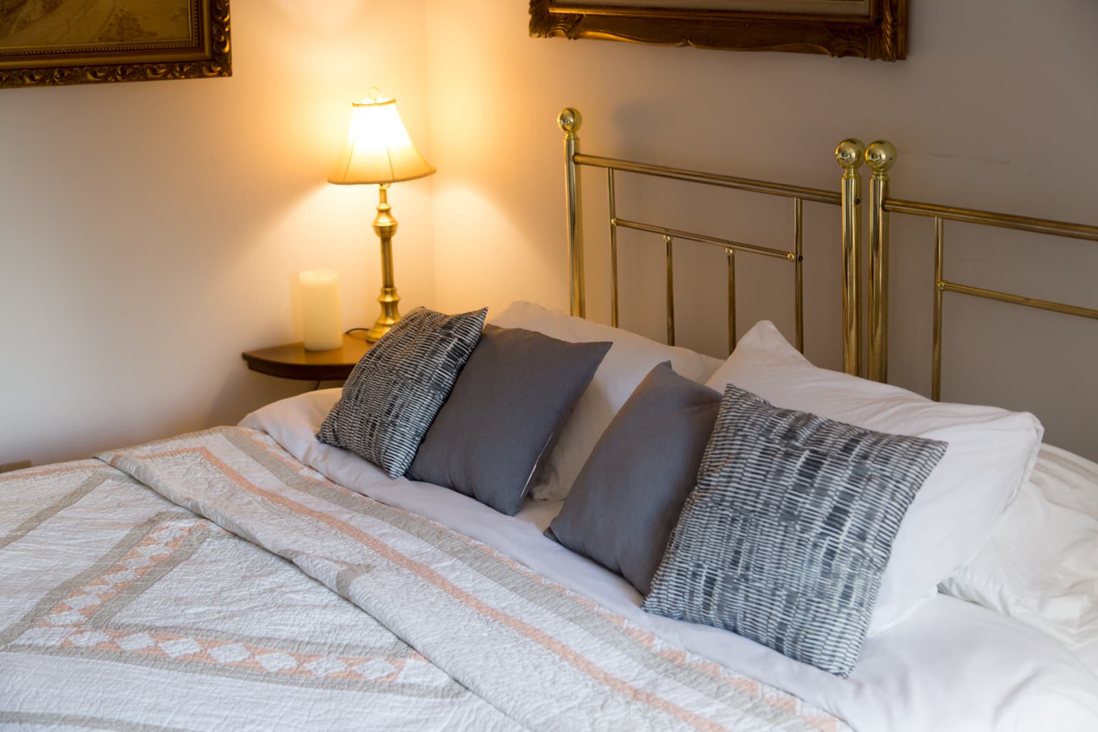 The king bed close up — brass bedstead, grey and woven cushions, and a brass lamp on the bedside table