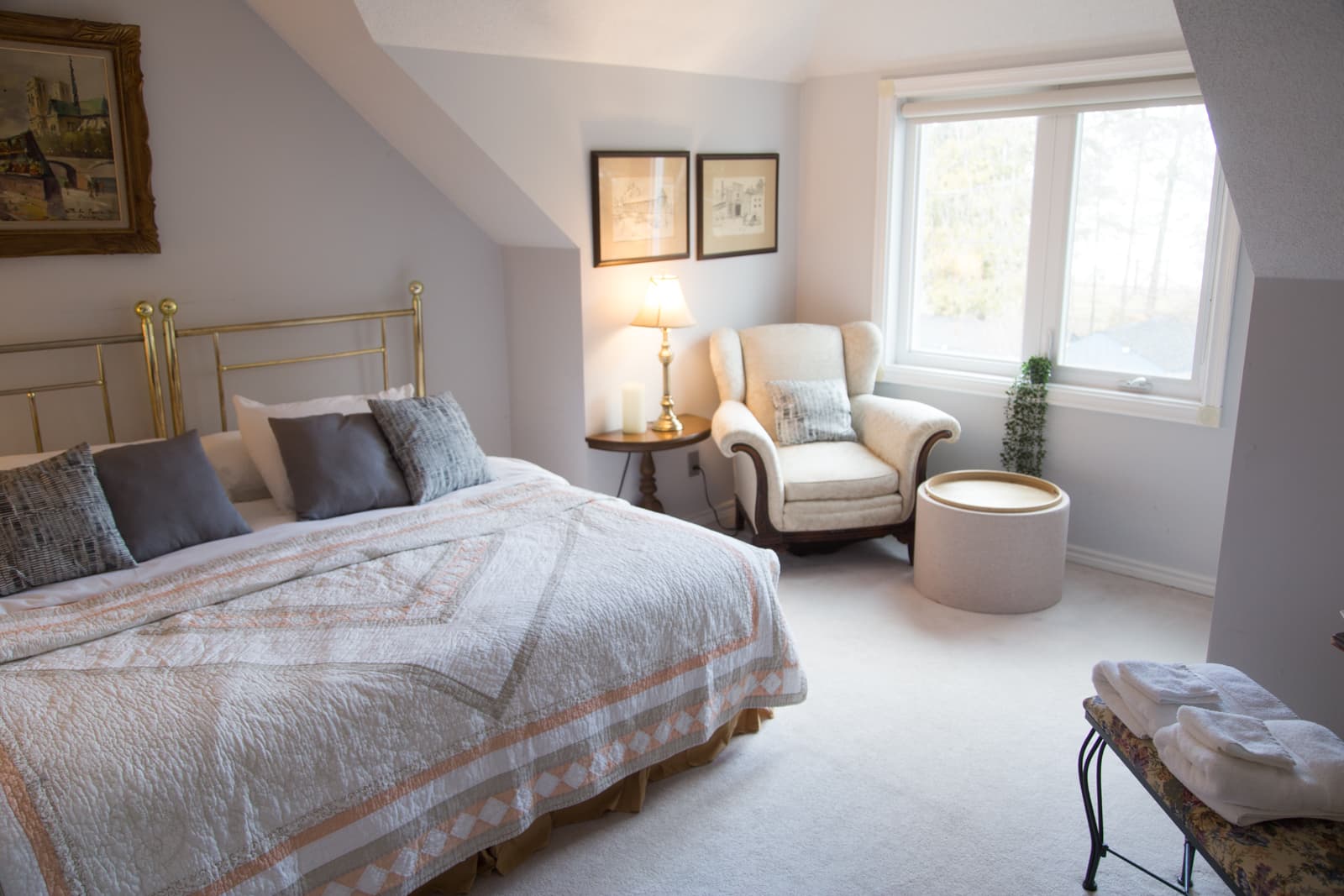 The Lakeview Room made up as a king bed, with a brass bedstead and cream quilt beside the wingback chair and window
