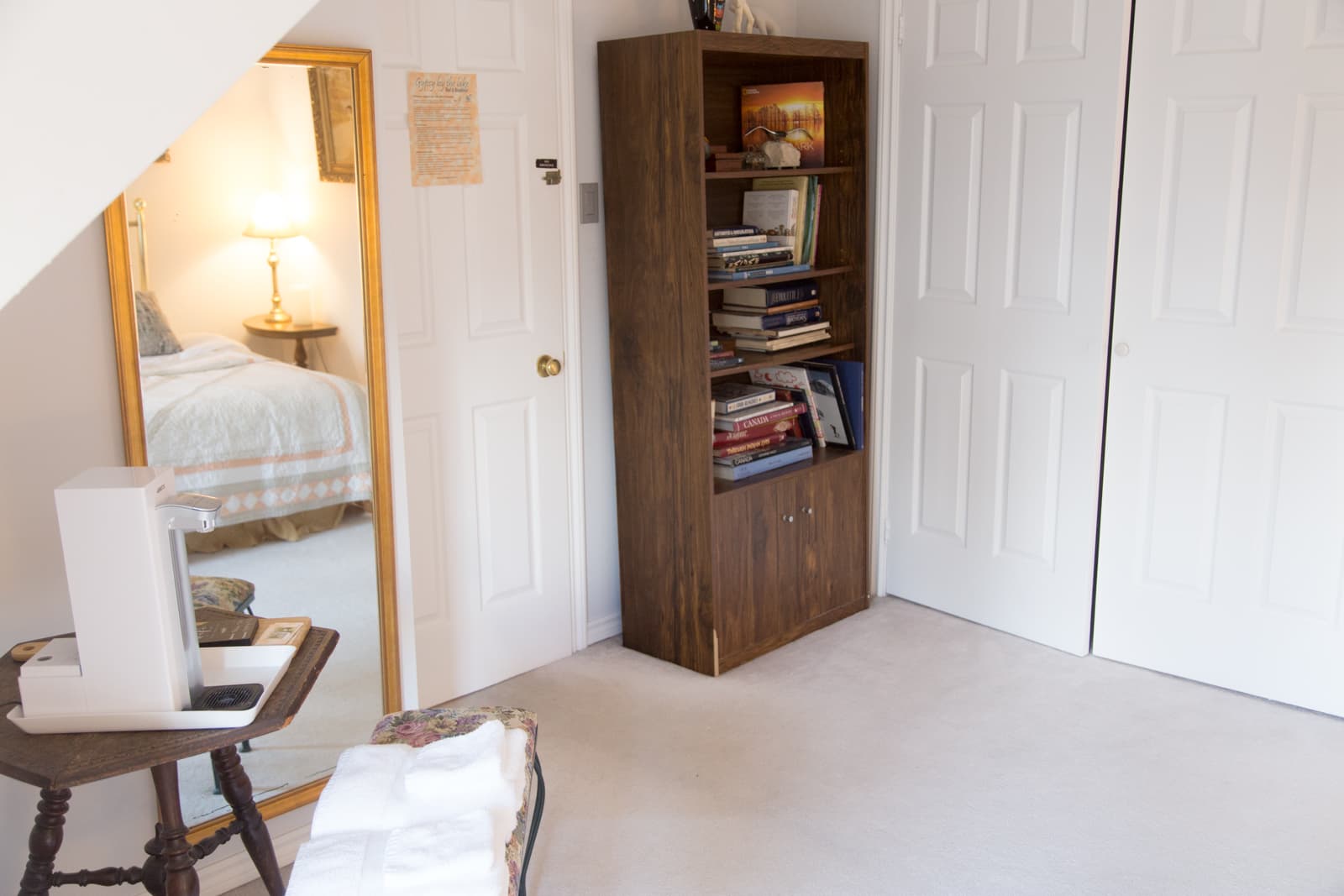 The corner of the Lakeview Room, with a full-length mirror reflecting the bed, a bookcase of books and the Brita water machine